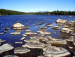 Rocks sticking out of low water and Mt Katahdin in the back.